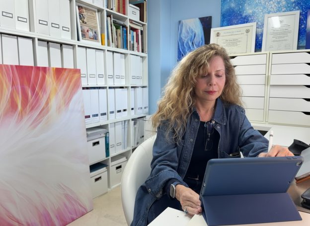 Mujer con cabello rizado usando una tablet en un despacho con archivos y arte en la pared.